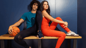 Homem e mulher vestindo roupas esportivas tecnológicas em poliamida com elastano, sentados em banco de vestiário, representando conforto, elasticidade e versatilidade no vestuário esportivo.