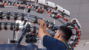 Colaborador operando maquinário industrial em indústria de tecido brasileira, com foco em produção têxtil tecnológica, eficiência produtiva e inovação industrial.