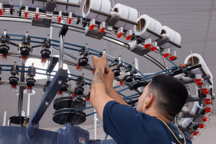Colaborador operando maquinário industrial em indústria de tecido brasileira, com foco em produção têxtil tecnológica, eficiência produtiva e inovação industrial.