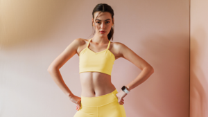 Modelo usando conjunto fitness amarelo suave com top e legging, representando as novidades da moda esportiva e tendências têxteis 2026 em performance e tecnologia.