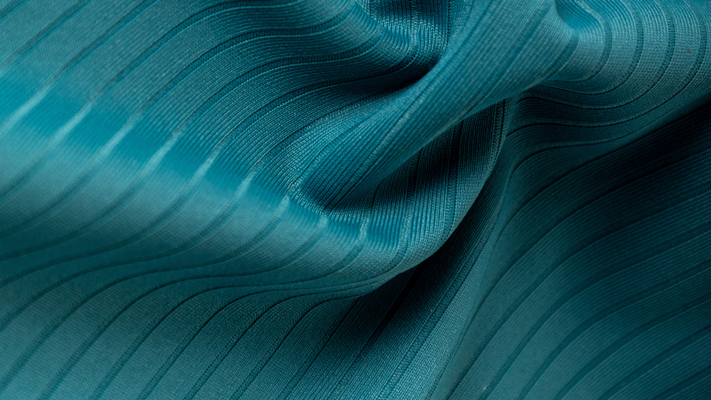 Tecido técnico azul-esverdeado com textura canelada e elasticidade, destacando estrutura e flexibilidade para roupas fitness de alta performance.