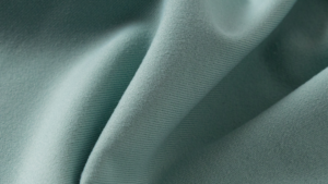 Close-up de um tecido de alta performance na cor verde suave, com superfície uniforme e toque macio, evidenciando a elasticidade, o conforto e a qualidade técnica do material utilizado na moda esportiva.