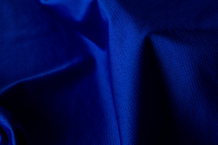 Close-up de tecido esportivo azul com textura técnica, destacando sua estrutura e acabamento voltados para durabilidade, conforto e caimento.