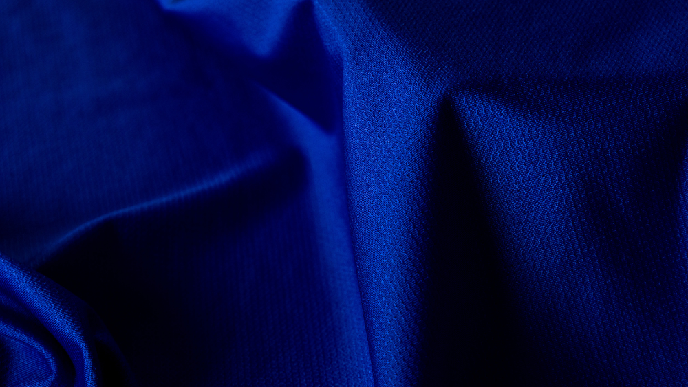 Close-up de tecido esportivo azul com textura técnica, destacando sua estrutura e acabamento voltados para durabilidade, conforto e caimento.