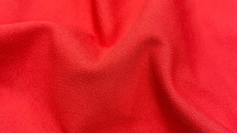 Tecido esportivo vermelho com textura e caimento para roupas de alta performance.
